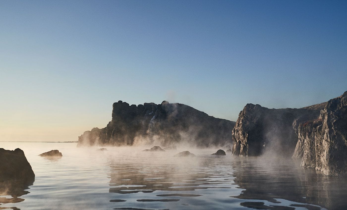 Gufa rís upp úr hlýju baðlóni Sky Lagoon innan um kletta með fallegu sjávarútsýni.